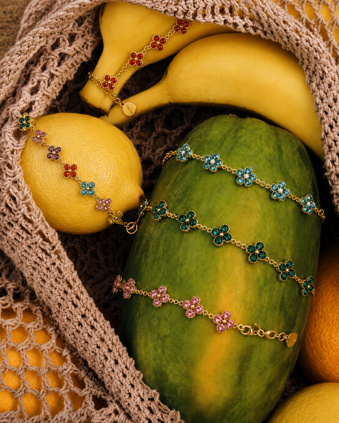 Bracelets fleur OMEYA Bloom dorés et colorés disposés sur des fruits dans une ambiance estivale